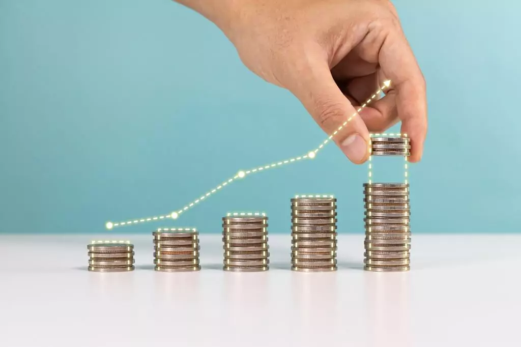 mão colocando moedas em pilha ao lado de pilhas menores