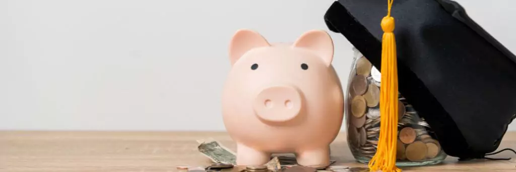 porquinho ao lado de vidro com moedas e capelo por cima