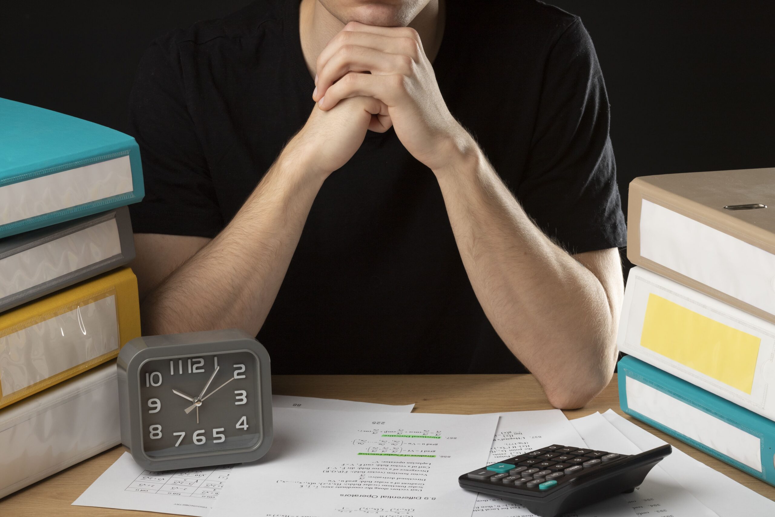 homem preocupado com suas dividas sentado em uma mesa com uma calculadora, papeis e um relógio sobre a mesa