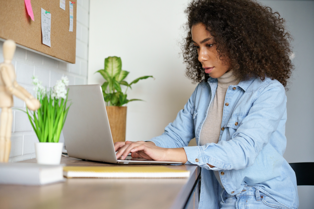 Mulher sentada em uma mesa com o seu notebook estudando