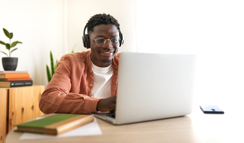 Homem sentado em uma mesa em sua casa estudando com o seu notebooks e livros