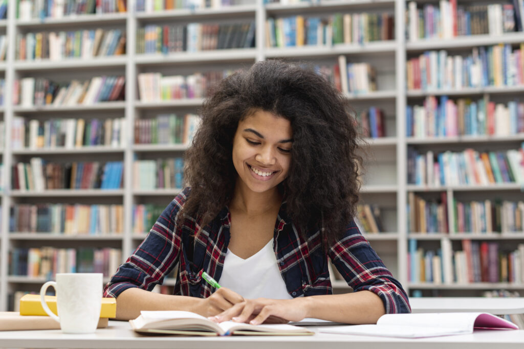 Garota sorridente na biblioteca da faculdade concentrada em seus estudos 